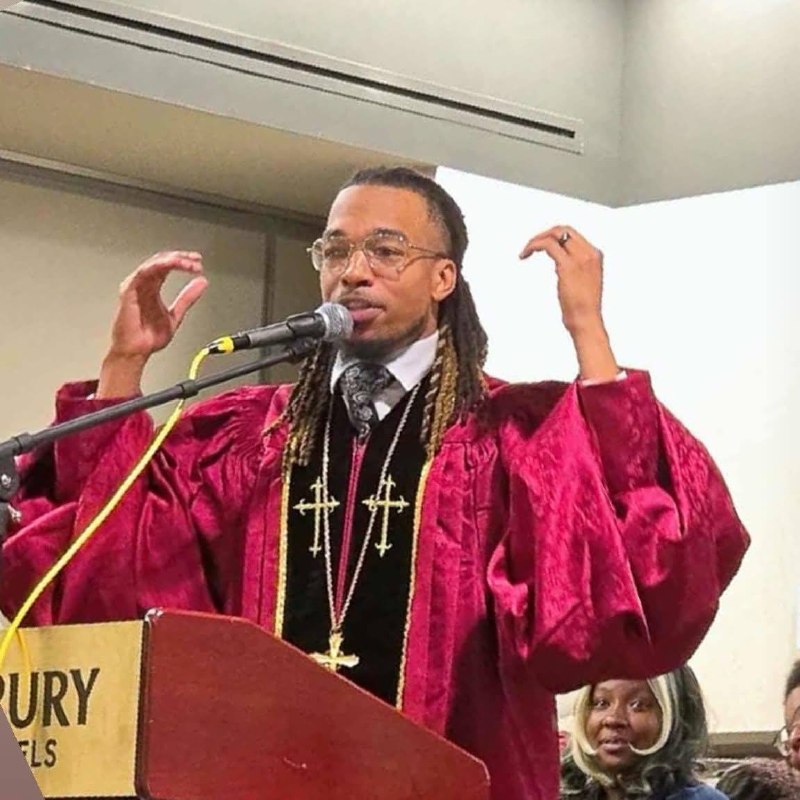 Apostle T.D. Robinson preaching in a maroon robe at the pulpit.